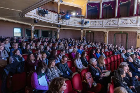 Na zdjęciu widoczna jest pełna sala konferencyjna w eleganckim, zabytkowym teatrze. Uczestnicy konferencji **"Culture for Health and Wellbeing"** siedzą w czerwonych fotelach, uważnie słuchając prelegentów. W górnej części kadru widać balkon z technikami obsługującymi sprzęt audiowizualny. Atmosfera skupienia i zaangażowania podkreśla rangę wydarzenia.